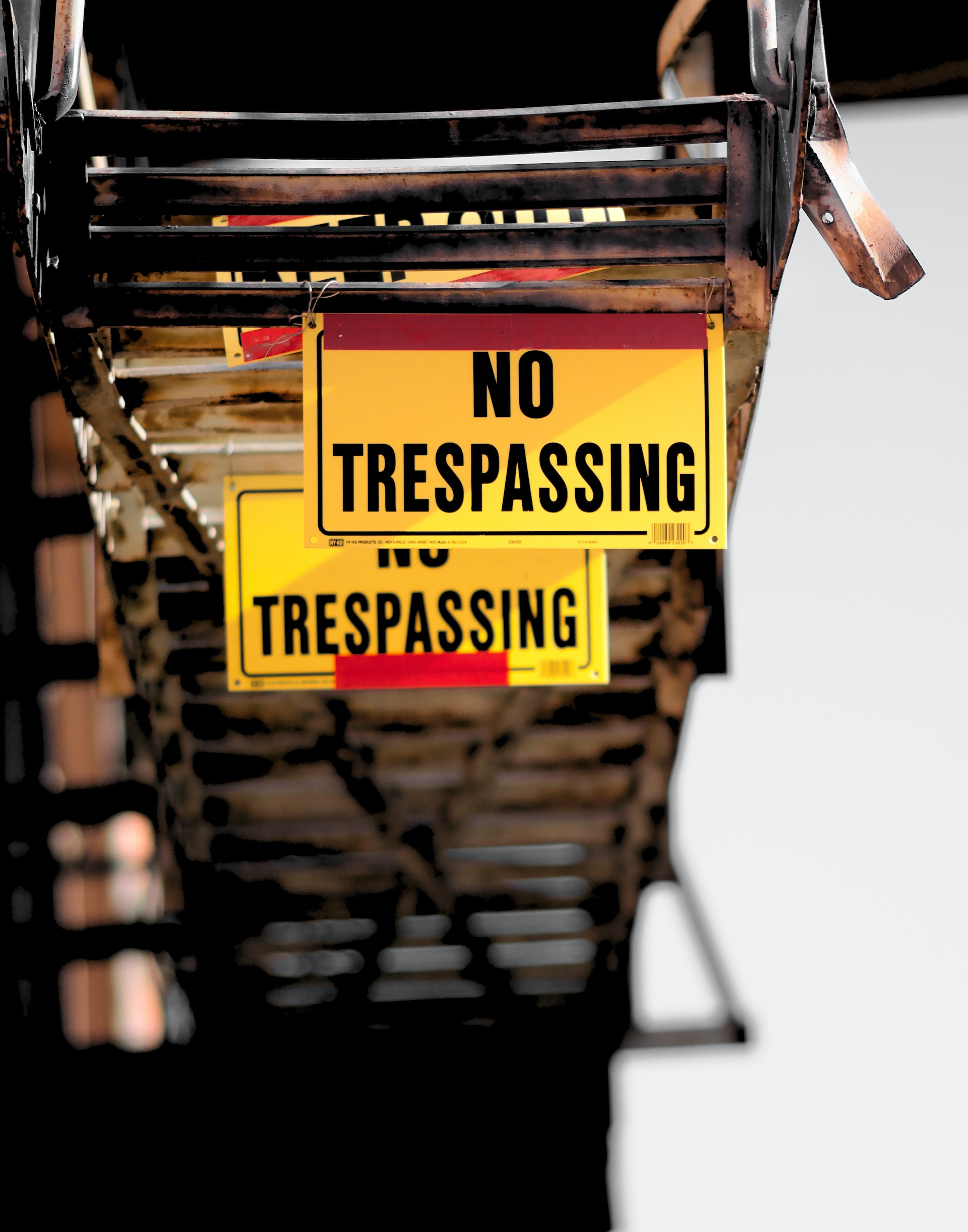Gelbes Schild mit der Aufschrift 'NO TRESPASSING' befestigt an einem rostigen Metallgitter, was auf Maßnahmen zur Perimeterkontrolle hinweist.